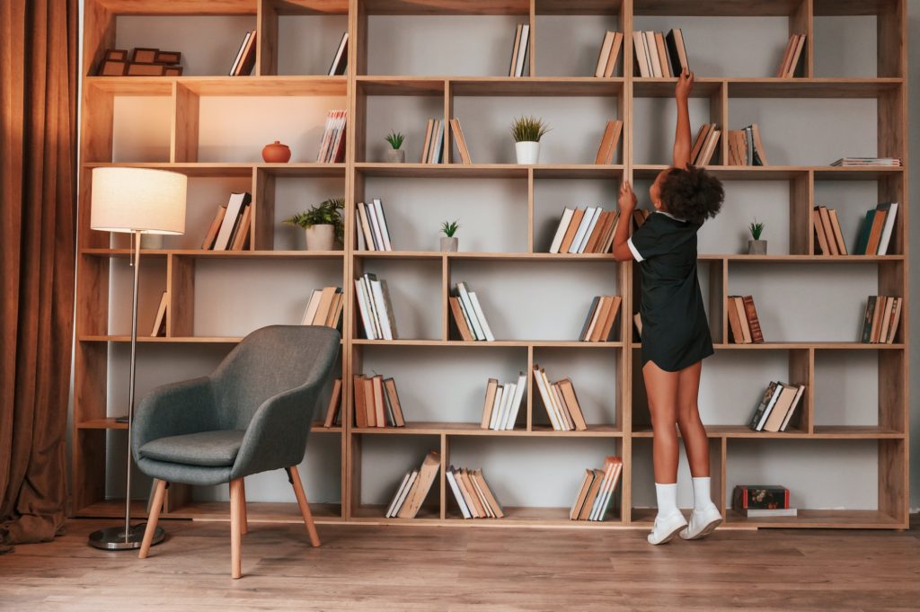 Searching for the books. Cute african american girl in school uniform is at home library